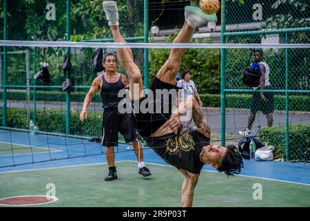 A Thai player of Sepak Takraw is seen performing an acrobatic figure during a game at Benchasiri Public Park on Sukhumvit Road. Sepak Takraw also called kick volleyball or Thailand’s Acrobatic Volleyball is one of Southeast Asia’s most popular sports which is played with a ball made of rattan or synthetic plastic where the players are only allowed to touch the ball with their feet, body, or head. Stock Photo