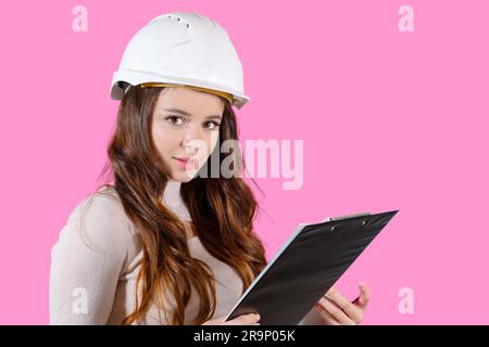 A young female engineer in a helmet holds her project in her hands on the pink background. Stock Photo