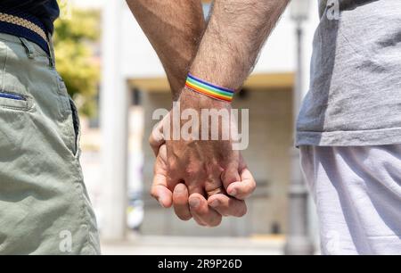 Close up of a male gay couple holding hands with a rainbow bracelet on one wrist. Gay pride concept Stock Photo