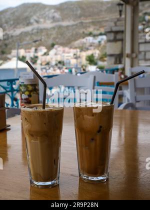 Symi, Greece - May 28, 2023: Two glasses of frappe iced coffee on a wooden table at sea coast café, Symi, Greece. Stock Photo