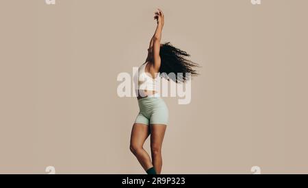 Fit woman standing in a studio in gym wear, moving her body with her arms raised. Young woman with a toned body sculpture showcasing her flexibility a Stock Photo