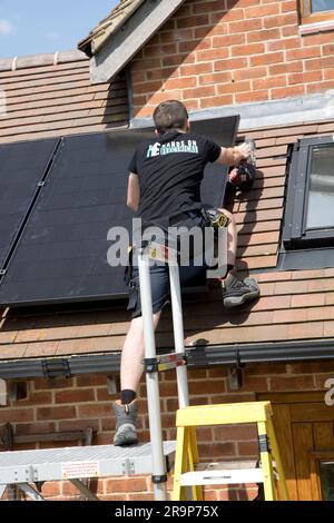 Technician installing black 410kW Perlite panels on tiled roof which already has  a set of evacuated  ET tubes for solar water heating at Colemans Hil Stock Photo