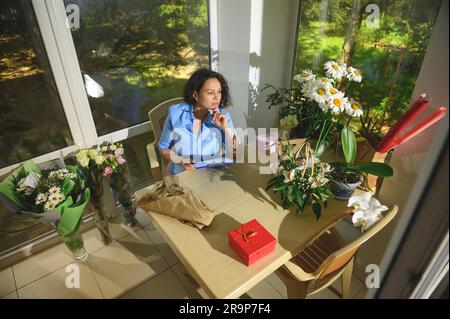High angle view woman florist decorator working on flower arrangements, sketching on clipboard in a floral design studio Stock Photo
