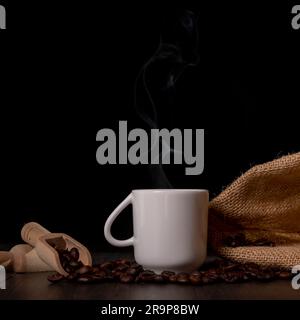 A cup of steaming espresso with coffee beans next to it Stock Photo