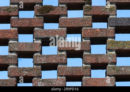 wall of open lattice bricklaying pattern with the blue sky peering though the spaces in the brickwork make a unique background, moss grows on some Stock Photo