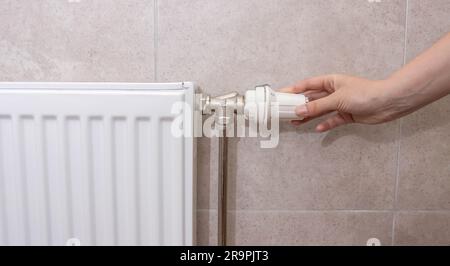 A woman regulates the gas heating in the room in order to save gas energy, taking into account the sanctions. Comfortable heating in the house. Stock Photo