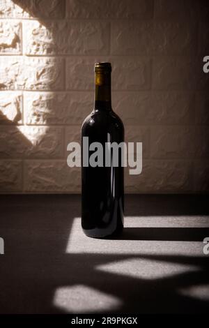 Unlabeled red wine bottle mockup on gray stone surface, textured white brick wall background. Diagonal long shadows. Minimalist concept. Stock Photo