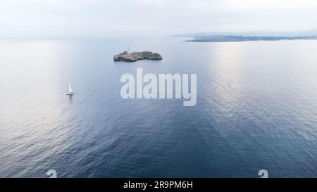 Aerial view of Cantabrian sea with clouds reflected in the water, Faro de Mouro lighthouse and sailboat. Early morning. Santander, Cantabria, Spain. Stock Photo