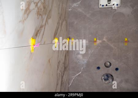 Laying modern large format tiles with the tile leveling system in the toilet. Laying tiles on the wall of the installation for the toilet. Stock Photo