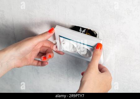 The girl is trying to insert a torn out socket from the socket due to the wrong pulling out of the electrical plug. Stock Photo