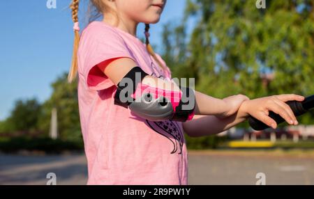 pink children's protection on the elbows of a girl who rides a scooter. Protection against falls and injuries. Close-up Stock Photo