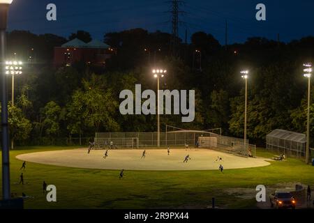 Play ball! A rec league baseball game is played under lights at a large park in Toronto on a fine summer evening Stock Photo