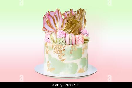 Beautiful pink and green cream cheese cake with rice paper, edible gold and macaroons. Delicious birthday cake isolated. Stock Photo