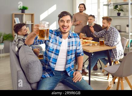Portrait of man holding glass of beer with a company of friends talking in the background. Stock Photo
