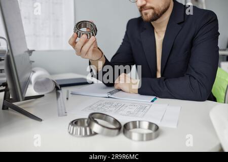 Closeup of mechanical engineer at workplace reviewing blueprints and holding machine part, copy space Stock Photo