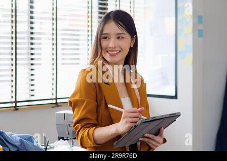 Female fashion designer woman working on her designs in workshop studio, Female business owner with clothes, Tailoring business owner, Clothing store Stock Photo
