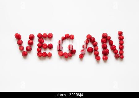 The word vegan is laid out from raspberries on a white background, no meat Stock Photo