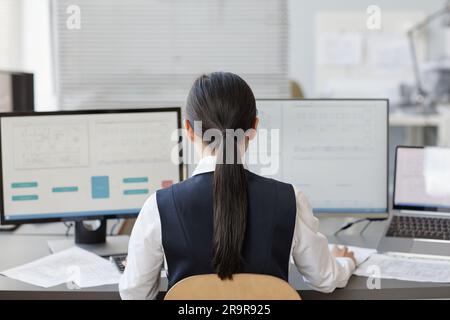 Back view of woman working as female engineer using computer with blueprints on screens, copy space Stock Photo