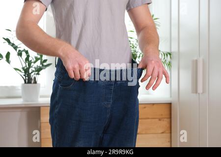 The guy is trying on big jeans after losing weight. Man in oversized pants in weight loss concept Stock Photo