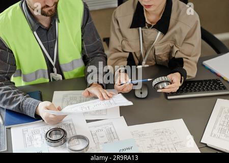 Top view at two engineers designing blueprints at workplace in office and holding machine part, copy space Stock Photo