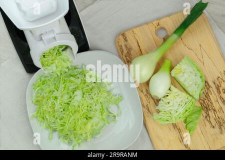 Cabbage in a vegetable cutter on kitchen table. Chopped cabbage is falling into a bowl. Homemade healthy food. Stock Photo