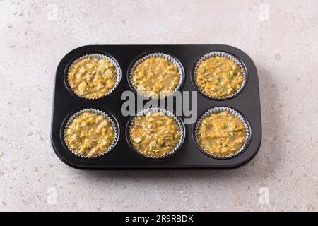 Raw dough for pumpkin muffins with oatmeal and nuts in a baking dish on a beige textured background. Cooking delicious healthy homemade cakes. Stock Photo