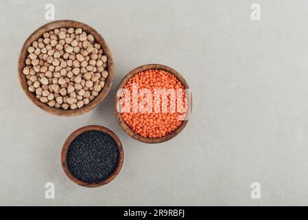 Dry raw organic red lentils, black sesame seeds and chickpeas in wooden bowl on concrete background. Top view Stock Photo