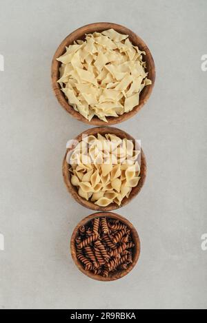 Three different types of pasta in wooden bowls on concrete background, top view. Stock Photo