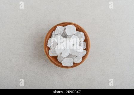 Close-up of organic crystalline rock sugar candy in wooden bowl on concrete background. Top view Stock Photo