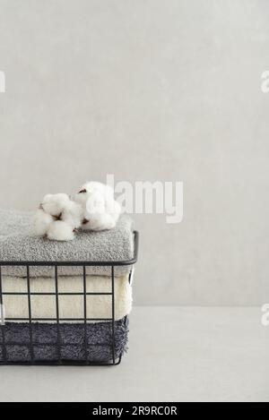 Stack of bath towels with cotton flowers in black metal basket on light concrete background closeup Stock Photo