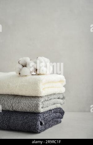 Stack of bath towels with cotton flowers on light concrete background closeup Stock Photo