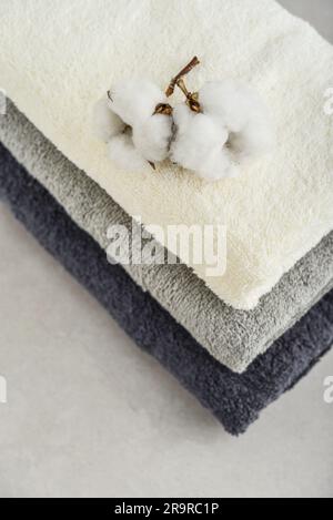 Stack of bath towels with cotton flowers on light concrete background closeup Stock Photo