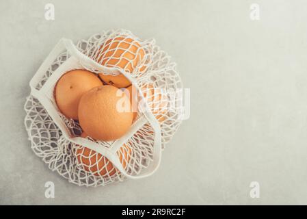 Cotton mesh bag with organic oranges on concrete background, top view Stock Photo
