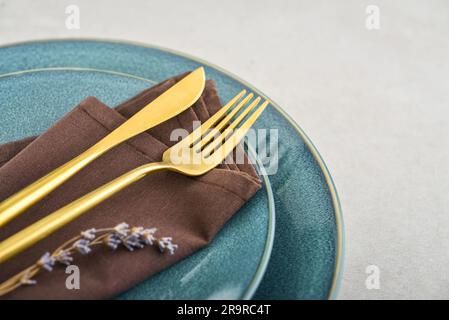 Modern minimal table place setting with blue plates and golden cutlery on gray concrete background . Modern kitchen. Stock Photo