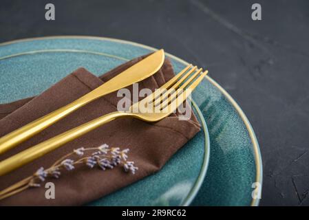 Modern minimal table place setting with blue plates and golden cutlery on black  background. Modern kitchen. Stock Photo