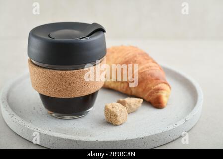 Coffee to-go in reusable travel mug made from glass and cork band with croissant on tray. Zero waste. Sustainable lifestyle concept. Stock Photo