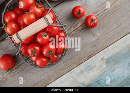 Cherry tomatoes in a vintage metal basket on a wooden background, top view Stock Photo