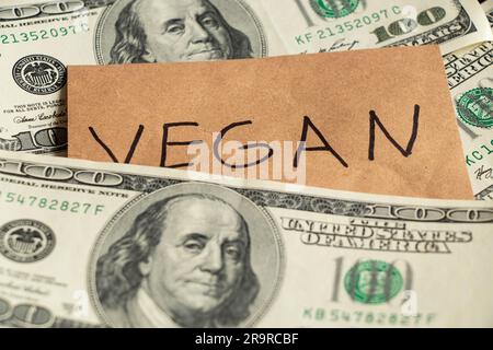 The word vegan is written on paper on the background of a one hundred dollar bill, the refusal of meat, the price of vegetables, business Stock Photo