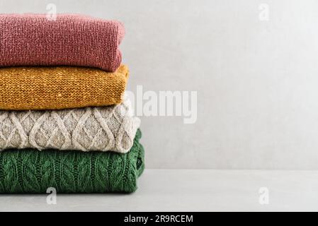 Pile of hand knitted winter clothes on light background: sweaters, knitwear, space for text Stock Photo