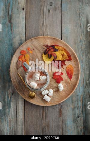 Cup of delicious hot cocoa with marshmallow and autumn colorful leaves on round wooden tray on wooden background, top view Stock Photo