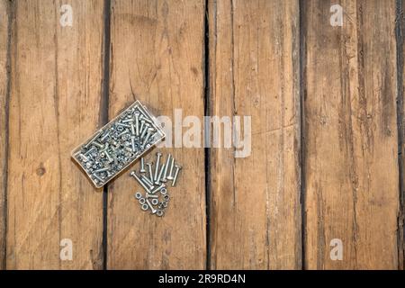 Nuts and bolts in a transparent box on the wooden floor. Screws. Old wood background. Stock Photo