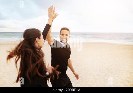 Smiling couple running giving high five on beach near ocean Stock Photo