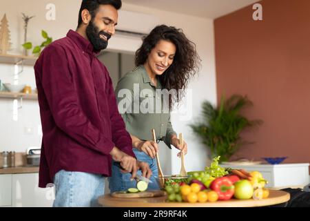 Healthy nutrition concept. Happy arab couple cooking fresh vegetable salad in kitchen together, copy space Stock Photo