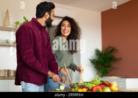 Joyful arab spouses cooking dinner and chatting, preparing fresh salad together in kitchen interior, free space Stock Photo