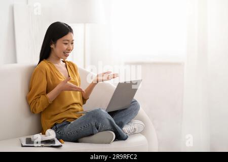 Positive asian woman working from home, using laptop Stock Photo