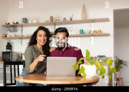 Happy arab spouses paying taxes online with laptop in kitchen, planning family budget or shopping online Stock Photo