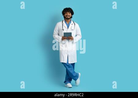 Cheerful indian doctor using digital tablet, blue background Stock Photo