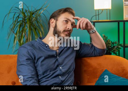 Sad lonely man sitting at home room looks pensive thinks over life concerns or unrequited love suffers from unfair situation. Arabian alone guy problem, break up, depressed feeling bad annoyed burnout Stock Photo