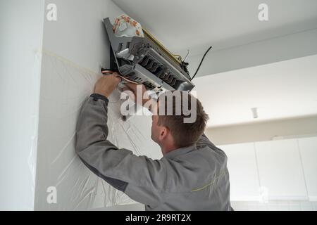 Professional man technician in uniform check installing air conditioner in modern apartment.  Stock Photo