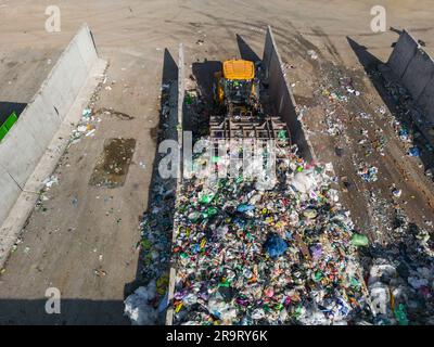 Skid steer loader moving plastic garbage with scrap grapple on the landfill site, drone shot. Waste disposal concept. Stock Photo